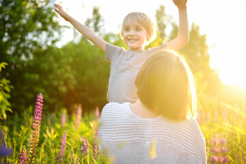 Charming woman with her little son walking and having fun in field of lupines on sunset. Outdoor activities for family with kids.