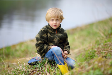 Preschooler child wearing yellow rain boots walking near river after rain. Kid playing and having fun on early spring day.