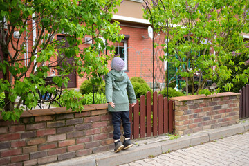 Fototapeta na wymiar Preschooler boy sniffing the lilac on street of small town on spring day. Kid exploring nature.