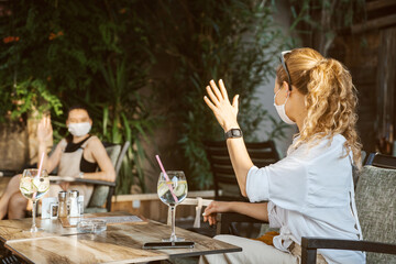 Women with medical facemask are greeting and keeping social distance in restaurant. Aftermath of...