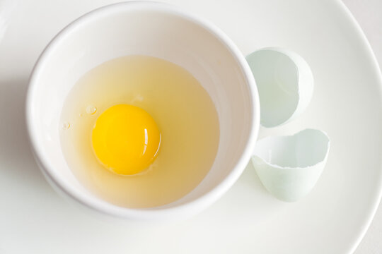 Raw whole egg in bowl and cracked eggshell on plate food ingredient