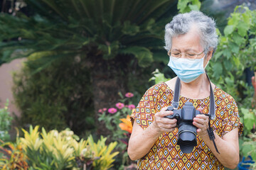 Portrait of an elderly woman wearing a face mask and holding digital camera