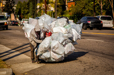 Man pushing shopping cart overloaded with white plastic bags filled with bottles and cans for recycling