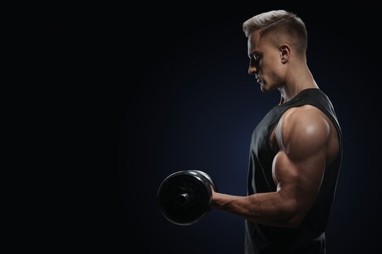 Athletic man in training pumping up muscles with dumbbell. Strong bodybuilder with perfect deltoid muscles, shoulders, biceps, triceps and chest. Close-up of a power fitness man.