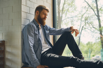 Young attractive bearded man rests and looks out the window. Enjoy the morning afternoon. Healthy...