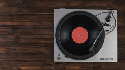 Fototapeta premium Vinyl record player on a brown wooden background. The view from the top.