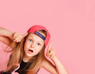 Little blonde female in cap and black blouse. She pointing up by forefingers and looking surprised,...