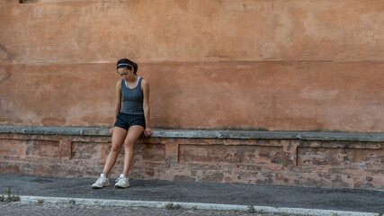 Young teen girl with headband, shorts, tanktop and sneakers sitting on brick bench