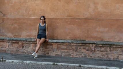 Young teen girl with headband, shorts, tanktop and sneakers sitting on brick bench