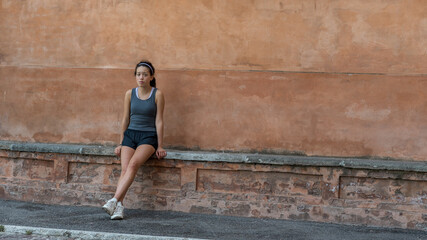 Fototapeta na wymiar Young teen girl with headband, shorts, tanktop and sneakers sitting on brick bench