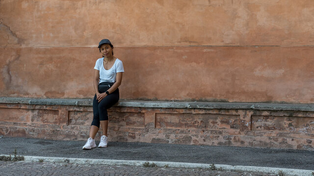 Woman in cap sitting on bench in front of beautiful teracota wall