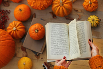 Naklejka na ściany i meble Autumn books.Learning and education concept.back to school. Halloween books. Open book in female hands on orange pumpkins background in bright sunshine.Cozy autumn mood . Fall season