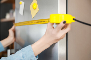Young woman measuring fridge in kitchen, closeup