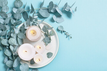 eucalyptus leaves and burning candles on blue background