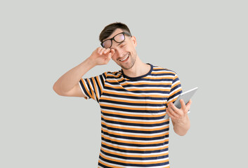 Tired man with tablet computer on light background. Concept of sleep deprivation