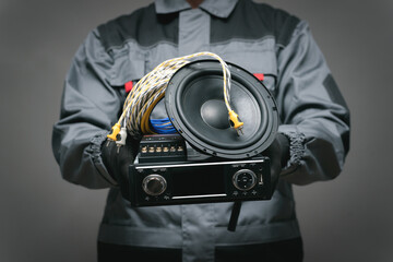 Car audio specialist holding in hands a car radio, loudspeaker and wires close up.