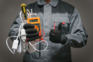 Electrician worker is holding in hands a multimeter with wires and is showing a thumbs up gesture close up.