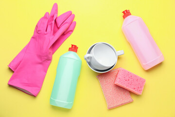 Cups, detergents, rubber gloves and sponges on color background