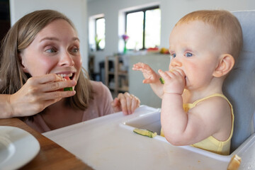 Happy excited mom training baby to bite solid food, eating watermelon together with daughter. Closeup shot. Child care or nutrition concept