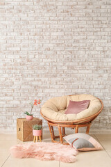 Fototapeta na wymiar Papasan chair with soft cushions near brick wall in room
