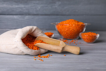 Bag and scoop with red lentils on wooden background