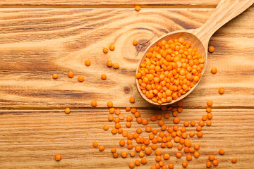 Spoon with red lentils on wooden background