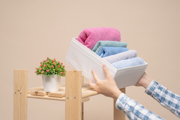 Woman is placing a bath towels in a storage box close up.