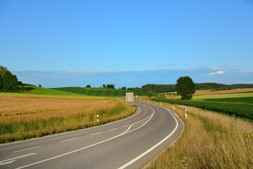 Fototapeta na wymiar In Bavaria in summer a road leads through the fields and forests against a blue sky