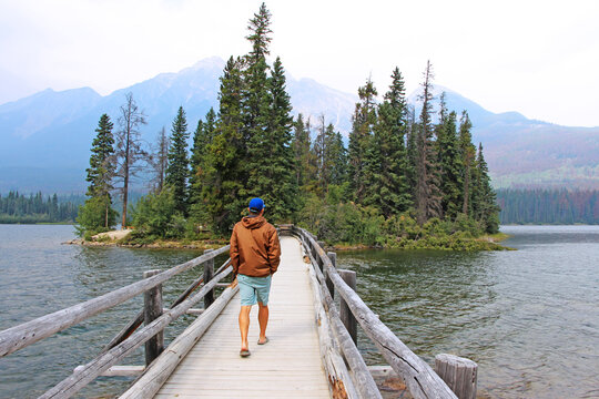 Man walking over the bridge to get to Pyramid island on Pyramid lake, Jasper National Park, AB. Pine trees in the background.