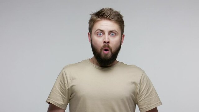 Wow, unbelievable! Bearded man feeling shocked astonished and looking big eyes surprised at camera, opening mouth in amazement, disbelief reaction on face. studio shot isolated on gray background