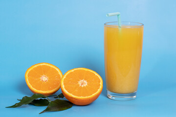 Fresh orange juice in a glass with fruit cut in half and sliced in green leaves isolated on a blue background copy space