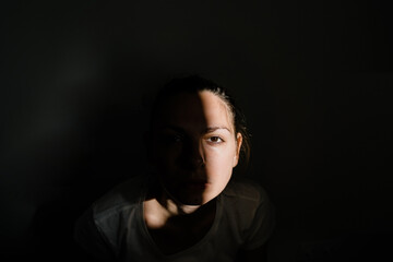 Girl sitting alone in sunlight pocket in dark room. mental health concept