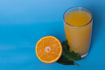 Fresh orange juice in a glass with fruit cut in half and sliced by green leaves isolated on a blue background, top view