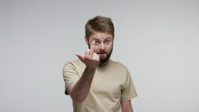 Aggressive hooligan bearded man showing middle finger, demonstrating protest hate with impolite rude gesture of disrespect, rejecting communication. indoor studio shot isolated on gray background
