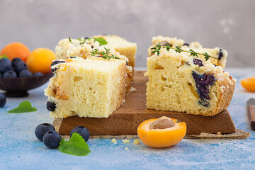 Blueberry and apricot crumble cake decorated with thyme on wooden cutting board. Blue stone background.