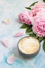 Morning cup of coffee or cappuccino and pink peonies on blue concrete table. Creative breakfast for Woman or Mother day.