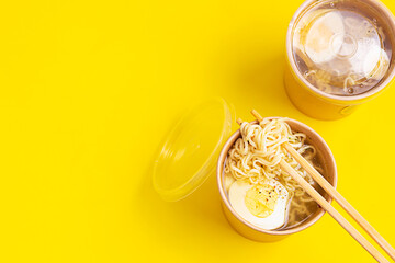 Chicken or vegetable broth with noodle and egg in craft containers on yellow background. Soup to go, healthy food delivery. Top view. Copy space.