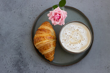Breakfast with coffee mug, fresh croissants and pink rose on grey stone background. Beautiful composition. Flat lay. Coffee concept. Top view.