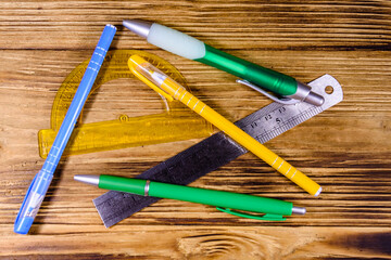 Multi colored ball pens, protractor and ruler on a wooden table. Top view