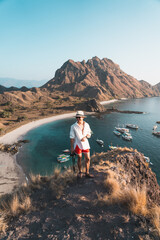 Young man traveller wearing white shirt standing on top of Padar island in a morning sunrise in summer season, Flores island in Komodo national park, Indonesia