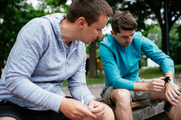 Fit young men taking rest from running. Two friends training outdoors.	