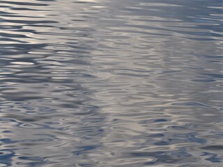 Peaceful and serene surface of lake or ocean, with ripples and waves, blue and silver colors. Good for background or wallpaper.
