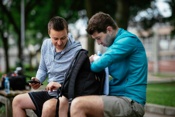 Fit young men taking rest from running. Two friends training outdoors.	