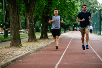Obraz premium Young men training on a race track. Two young friends running on the athletics track