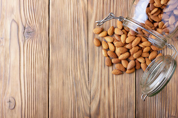 Almonds in a glass jar scattered on an old wooden table in cracks. Photo, image.