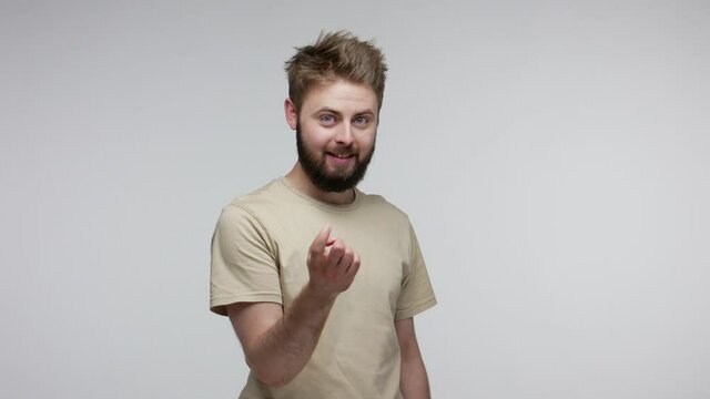 Hey you, come here! Handsome playful bearded guy gesturing one finger beckoning gesture, looking at camera winking and flirting, inviting hither. indoor studio shot isolated on gray background