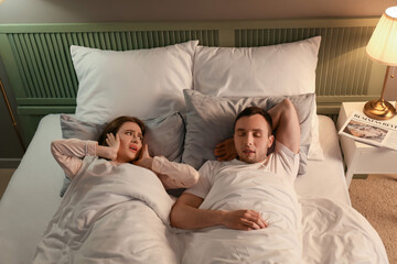Young irritated woman in bed with snoring husband
