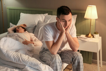 Young irritated man in bed with snoring wife