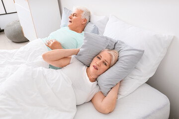 Mature irritated woman in bed with snoring husband