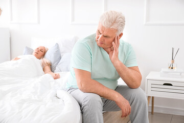 Mature irritated man in bed with snoring wife